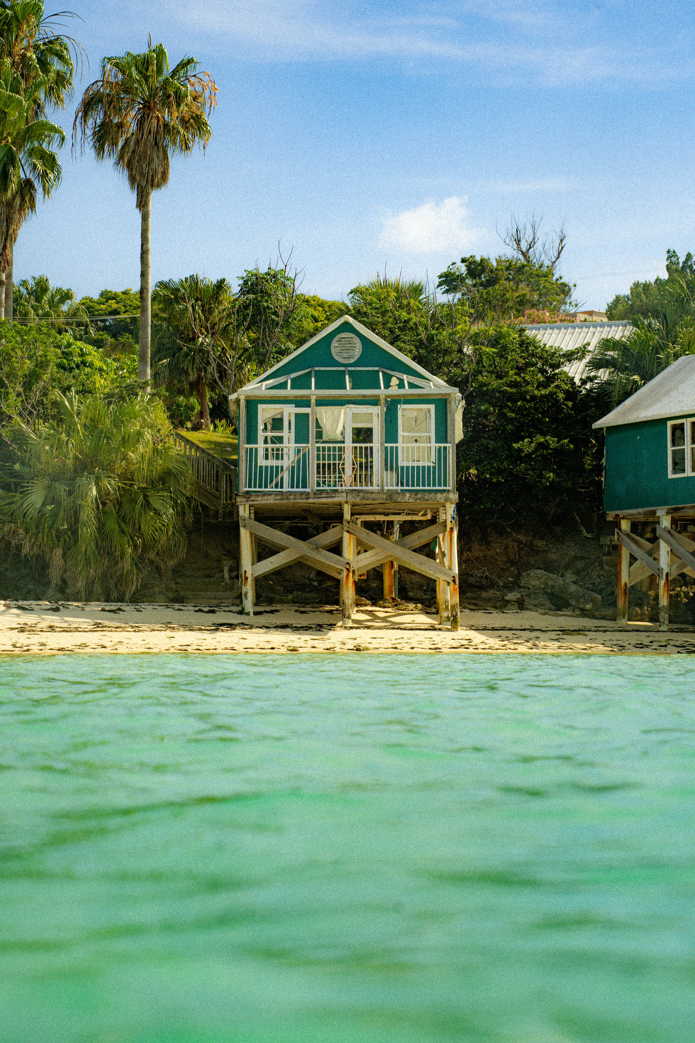 Teal beach cottage on stilts with white sand and turquoise water